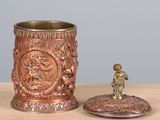 a small figurine sitting next to a cup on a table
