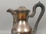 cafetière plaquée argent avec des motifs décoratifs, posée sur un socle, sur fond gris