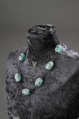 Collier de perles vertes et blanches sur un mannequin devant un fond noir