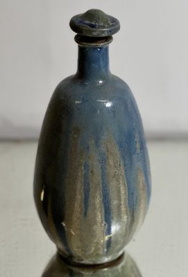 un petit vase bleu posé sur une table, avec un mur blanc en arrière-plan