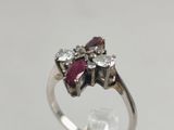 a close up of a diamond and ruby ring on a clear surface