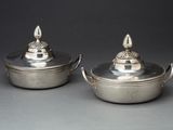 une paire de plats en métal argenté avec couvercles et poignées, posés sur une table