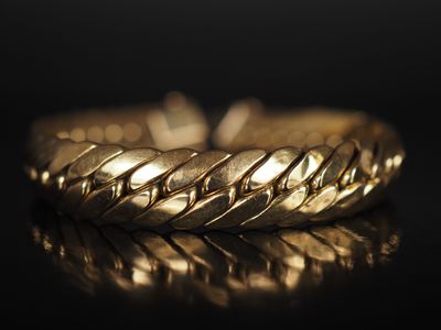 gros plan d'un bracelet en or sur une surface noire