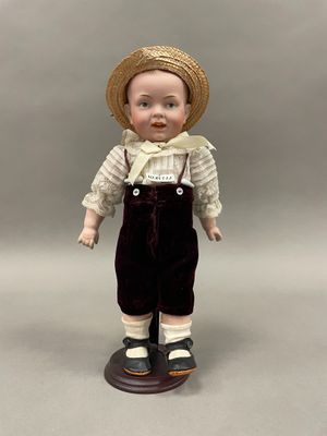 poupée en porcelaine représentant un petit garçon portant un chapeau de paille et une salopette