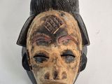 a wooden mask hanging on a wall on a white wall
