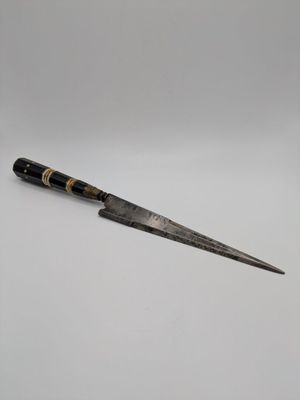 un gros plan d'un couteau posé sur une surface blanche, avec un fond gris