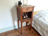 une petite table en bois sur laquelle est posée une lampe, à côté d'un lit