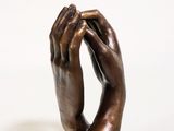 statue représentant une main tenant une bague, posée sur un socle en bois