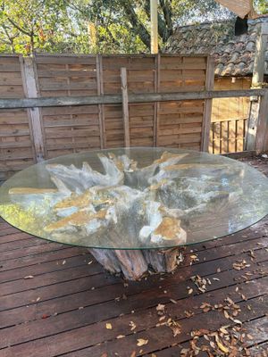 une table en verre sur une terrasse en bois, avec des feuilles par terre