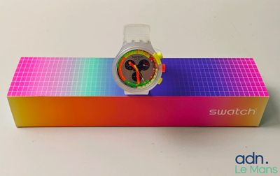 Montre Swatch dans son coffret, posée sur une surface blanche avec un fond arc-en-ciel