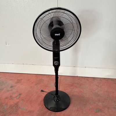 un ventilateur noir posé par terre devant un mur blanc