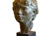 sculpture représentant une tête posée sur un socle en bois, sur fond blanc