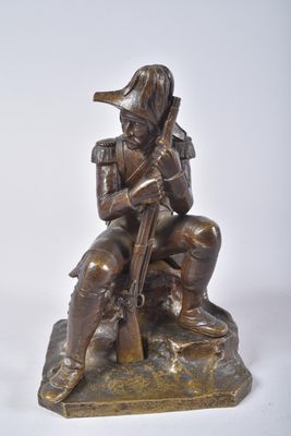 bronze statue of a man sitting on a rock with a rifle
