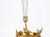 un vase en verre avec un socle doré et un animal doré représenté dessus