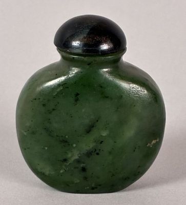 a green glass bottle with a black lid on a white surface