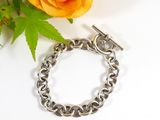 a silver chain bracelet on a white surface next to a rose