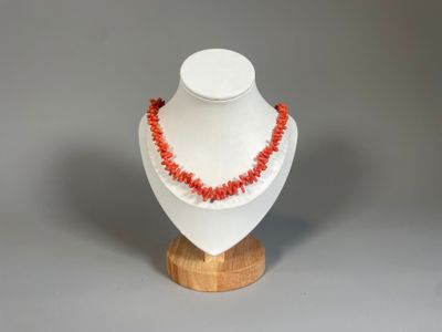collier composé de perles de corail rouge montées sur un support en bois, sur fond gris