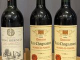 three bottles of wine sit on a wooden table in front of a gray wall