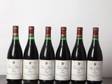six bottles of red wine lined up on a wooden table
