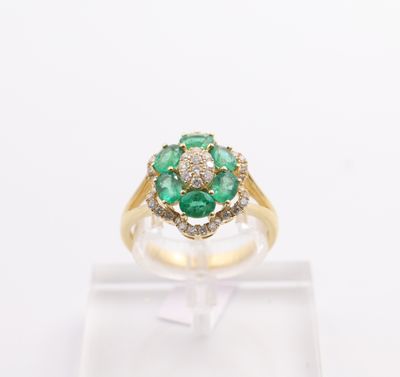 an emerald and diamond flower ring on a clear display stand