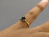 la main d'une femme, à laquelle est passée une bague sertie d'un diamant noir