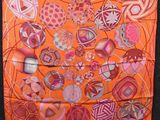 an orange scarf with a bunch of different designs hanging on a wall