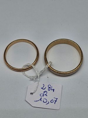 two gold wedding rings with a price tag on a white surface