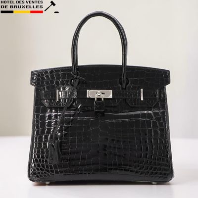 Le sac à main en cuir d'alligator noir est posé sur une table blanche.