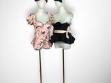 two mannequins dressed in black and pink dresses stand on a gold stand