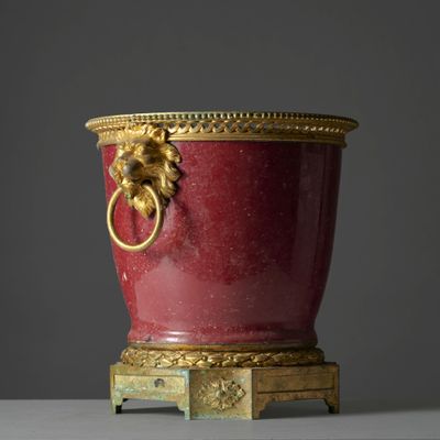 a red vase with a gold handle on a stand