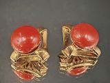 une paire de boucles d'oreilles rouges et dorées posées sur un fond noir
