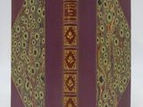 an old book with a red cover and gold trim on a white surface