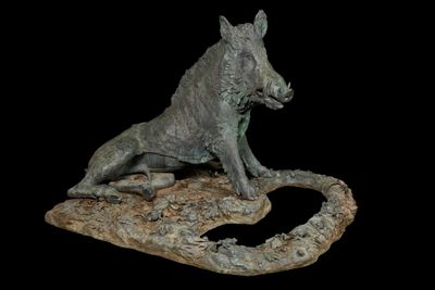 statue of a wild boar sitting on a rock with a black background