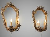 pair of gilded mirrors with candles on a stand in front of a gray wall