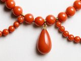 an orange beaded necklace with a tear shaped pendant on a white surface