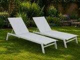 two white chaise loungers sitting in the grass in a garden