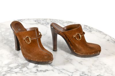 une paire de sabots en cuir marron posés sur une table en marbre, sur fond blanc