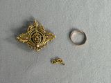 une broche en or et une bague posées sur un tissu gris
