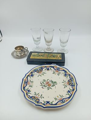 a plate with a flower design on it next to four glasses and a candle holder