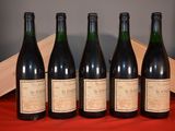 six bottles of wine are lined up on a red cloth
