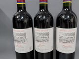 trois bouteilles de vin rouge sont alignées sur une surface grise