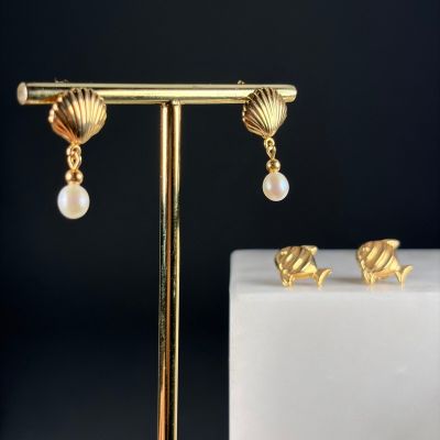 a pair of gold earrings with pearls and seashells on a stand
