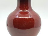 un vase rouge posé sur une table, sur fond blanc