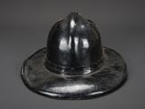 an old black fireman ' s helmet on top of a metal plate
