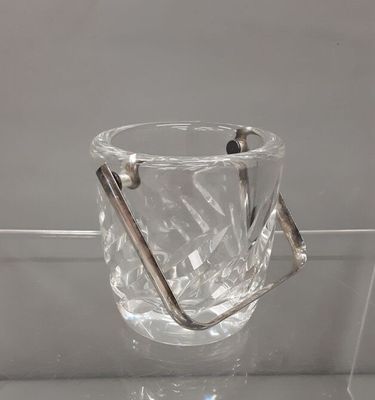 a clear glass vase with a metal handle on a glass shelf
