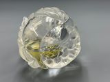 clear glass sculpture of a flower with a yellow center on a gray surface