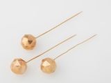 three gold plated metal balls on a white surface with a pair of needles