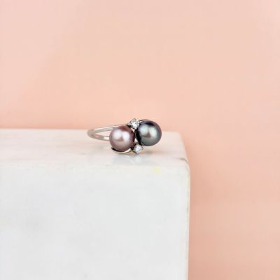 a black pearl and diamond ring sitting on top of a white marble block