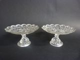 pair of clear glass footed dishes on pedestals on black background