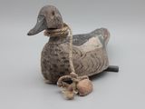 un canard assis par terre, avec une corde autour du cou